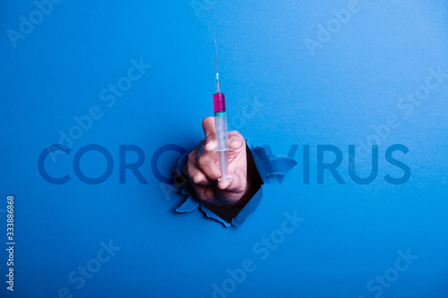 Human hand breaking a blue paper, in the hand is a syringe with the medicine against the coronavirus, concept in the fight against the coronavirus photo