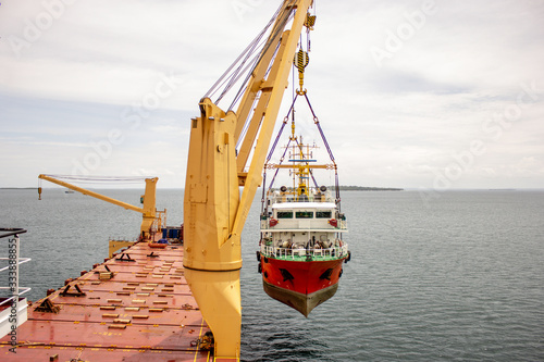 a scientific ship is loaded onto a deck of a heavy lift vessel  by tandem of two cranes with a pontoon installed