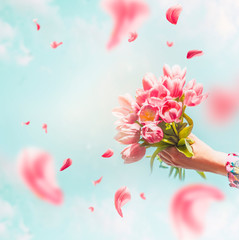 Female hand holding tulips bunch with flying petals at blue sky background. Creative greeting. Mothers day concept. Springtime abstract