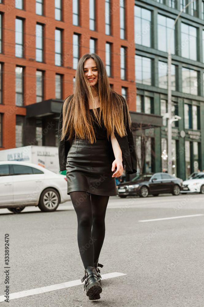 Full length portrait of attractive lady in formal clothes walking down the street with a smile on her face. Young beautiful business woman walking around the city, looking at the camera and smiling