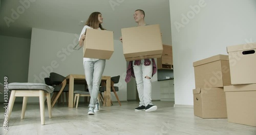 Young couple arriving in apartment with boxes. Man and woman in their 20s carrying cardboard boxes into new house. Slow motion, hand-held shot, wide shot, 4K.