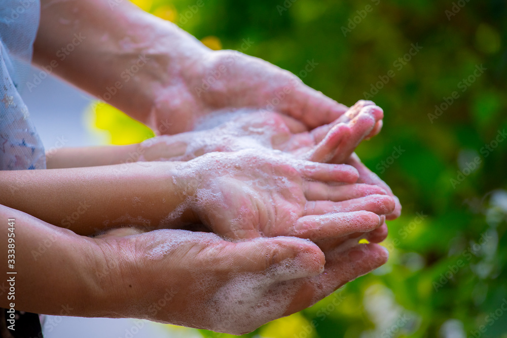 Mother and child washing hands with soap and water on green blur background.