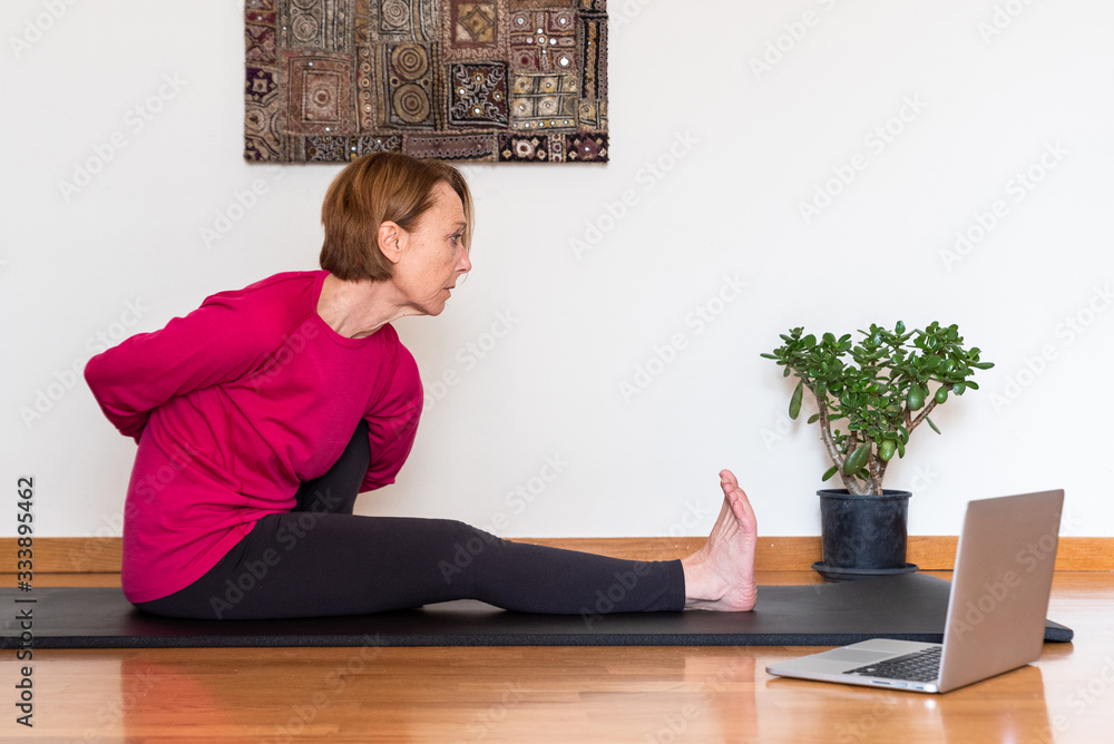 Middle aged woman watching yoga exercises online video tutorial on her laptop. Yoga at home concept. Middle aged woman watching yoga exercises online video tutorial on her laptop. Yoga at home concept.