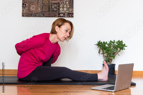 Middle aged woman watching yoga exercises online video tutorial  on her laptop. Yoga at home concept. photo