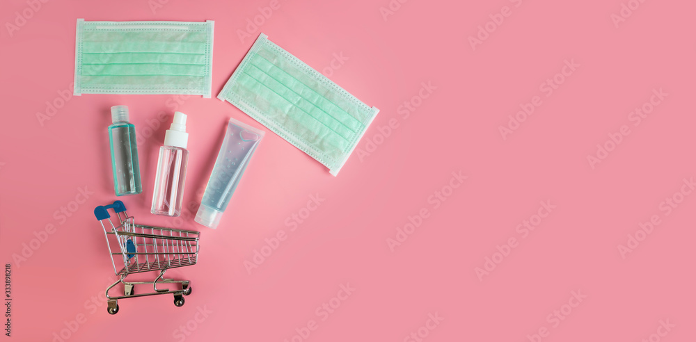 Fototapeta premium Small shopping cart and medical items to protect spread infectiously. Surgical mask, Alcohol gel and Alcohol spray on pastel pink background banner. Healthcare and shopping online concept, copy space