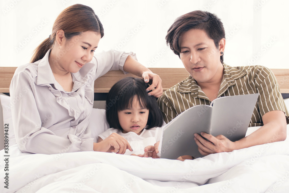 Dad and mom are reading bedtime stories to daughter