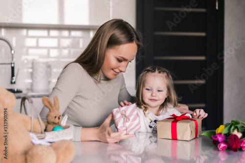 Young pretty mother and daughter with gifts box in the kitchen. Present concept.