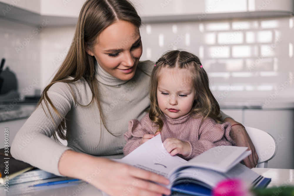 Young mother and child daughter doing homework writing and reading at home Young mother and child daughter doing homework writing and reading at home