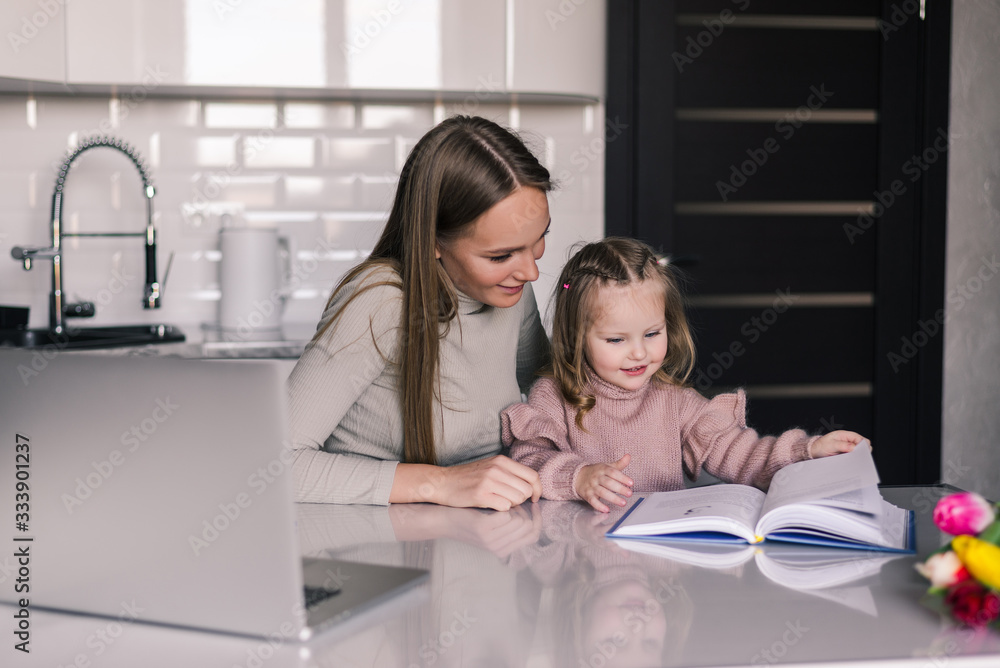 Mother and daughter reading book sitting at home at the table. Mother and daughter reading book sitting at home at the table.