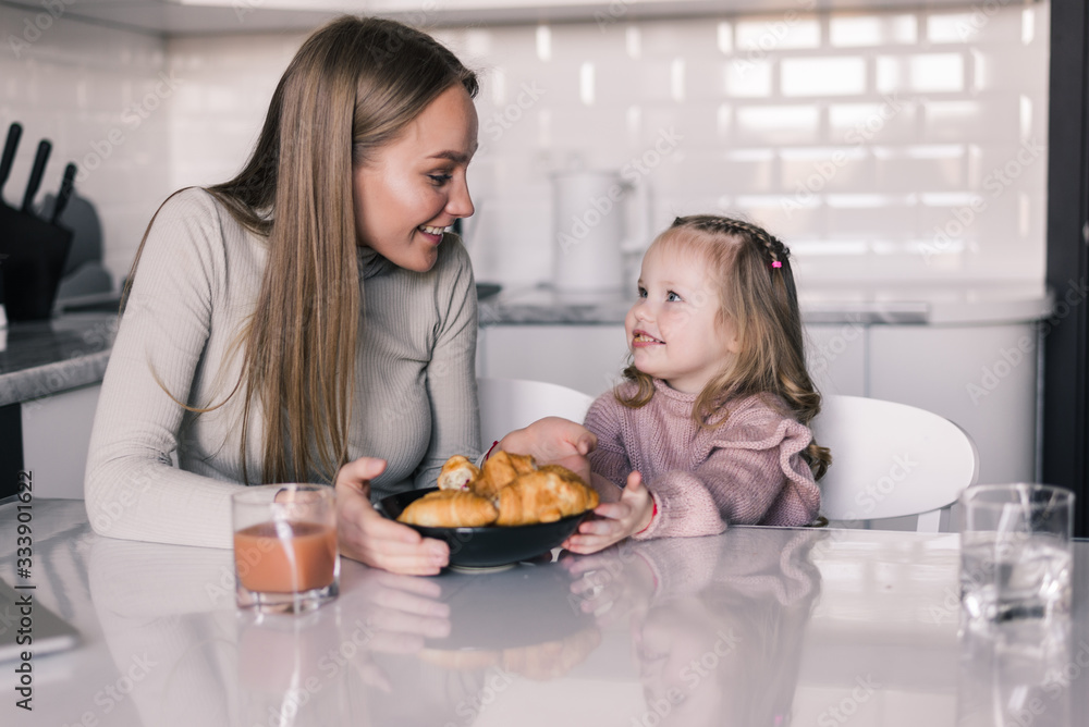 Breakfast at home. Happy family in the kitchen. Mother and child daughter are having breakfast with croissant and juice.