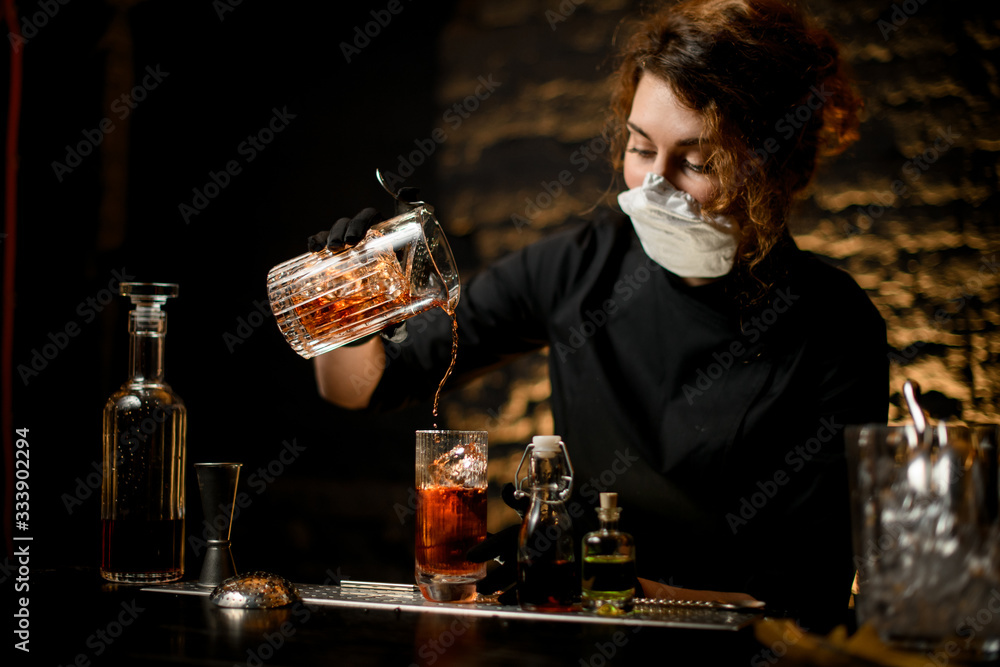 young woman at bar accurate pours cold cocktail into glass.