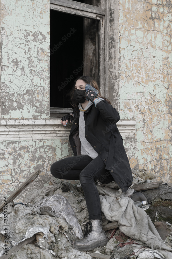 Teenager girl in a black medical mask with a children's gun, on the background of an abandoned post apocalyptic building.Consequences of COVID-19 Coronavirus protection. After a pandemic