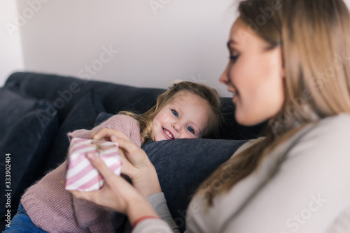 Young mother sitting on the couch at home received a surprise from her daughter looking at the gift in amazement in mother's day.