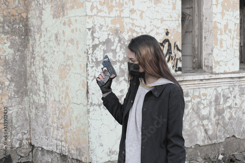 Teenager girl in a black medical mask with a children's gun, against the background of an abandoned post-apocalyptic building. Consequences of COVID-19 Coronavirus protection. After a pandemic