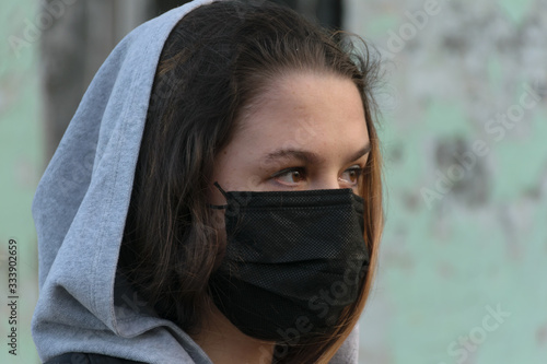 Young beautiful woman in a medical mask, looks into the distance on the background of an abandoned building. Consequences of COVID-19 Protection against coronavirus. Portrait of a Teen Girl. 