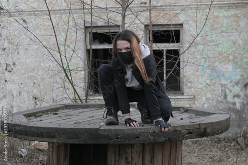 Teen girl in a black medical mask, In an abandoned post-apocalyptic building. Consequences of COVID-19 Protection against coronavirus. After a pandemic.