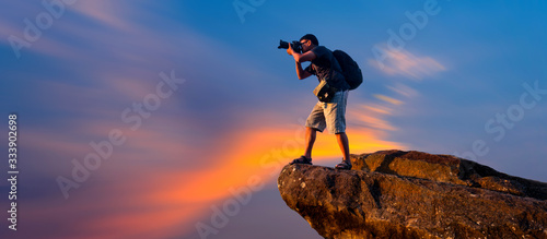 A photographer standing on top of Mountain at sunset with vivid clouds.