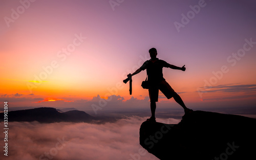 A photographer standing on top of Mountain at sunset with vivid clouds.