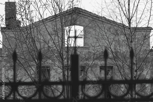 Abandoned and destroyed building behind a fence with a cross. Abandoned post-apocalyptic building