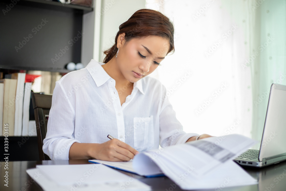 Beautiful Asian business women checking document and using notebook for working at home Beautiful Asian business women checking document and using notebook for working at home