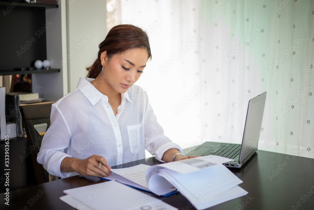 Beautiful Asian business women checking document and using notebook for working at home Beautiful Asian business women checking document and using notebook for working at home