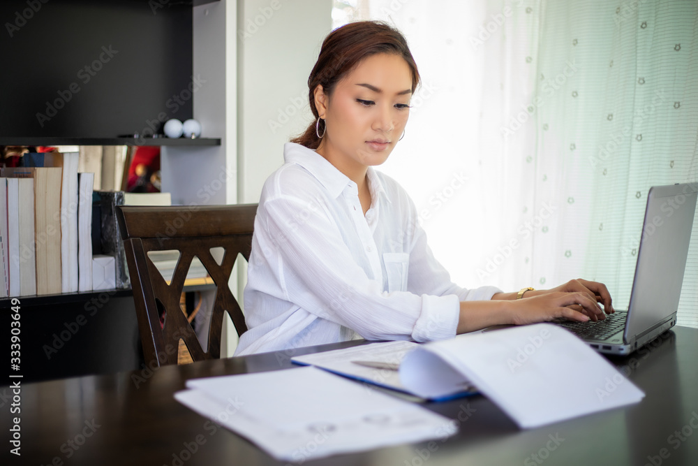 Beautiful Asian business women checking document and using notebook for working at home Beautiful Asian business women checking document and using notebook for working at home