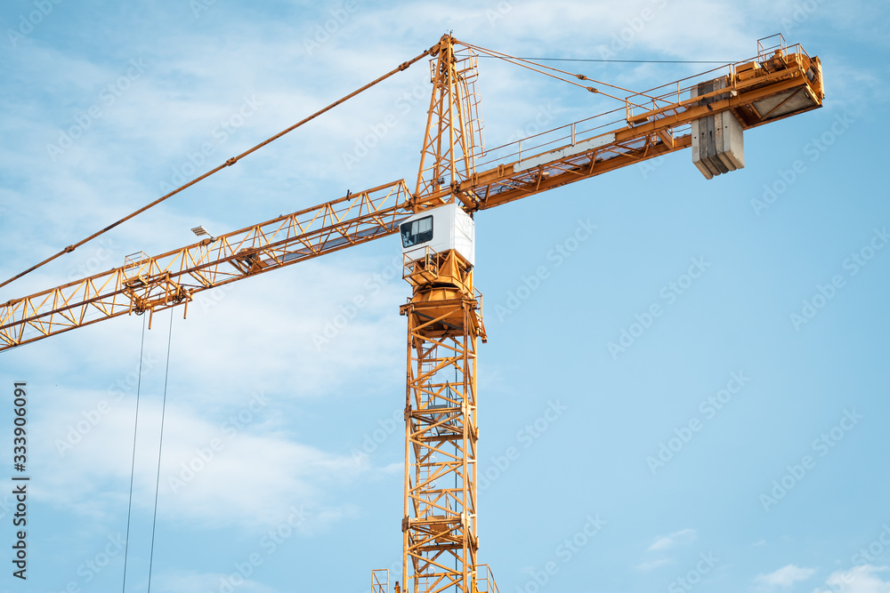 Yellow construction crane with cabin against blue sky. Lifting of cargo. Construction machinery concept, modern technology. Yellow construction crane with cabin against blue sky. Lifting of cargo. Construction machinery concept, modern technology.