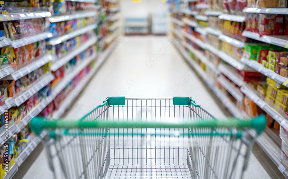 Blurred effect in the Supermarket aisle with empty silver and green shopping trolley,