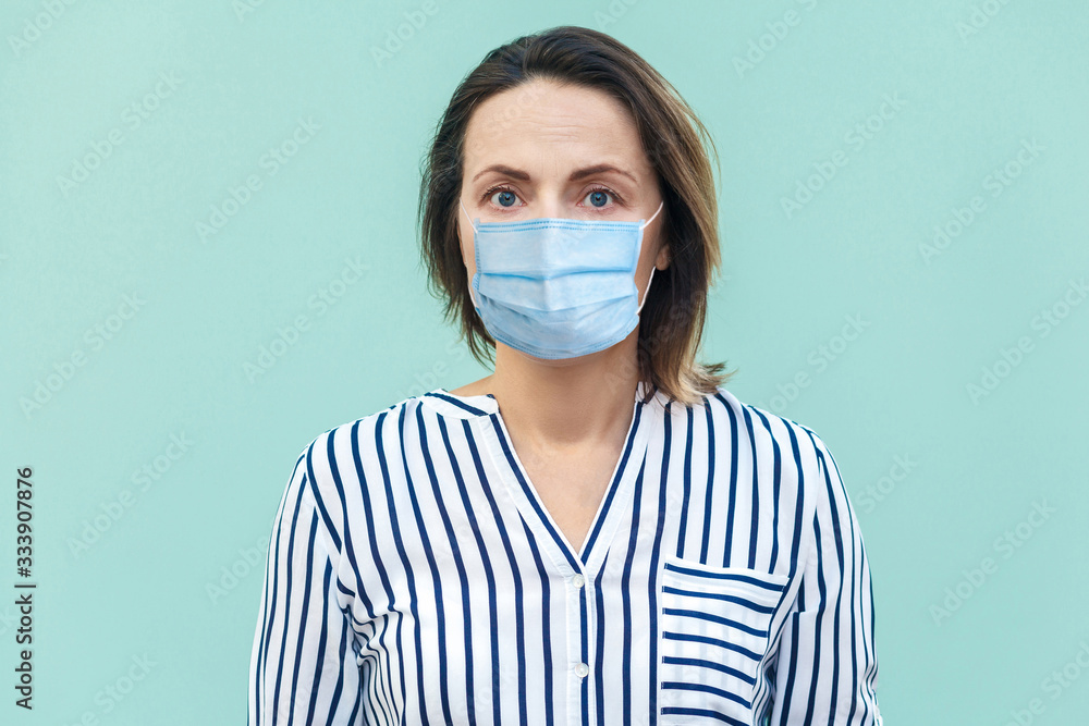 Portrait of serious middle aged woman with surgical medical mask standing and looking at camera. medicine and health care concept. indoor studio shot isolated on blue background. Portrait of serious middle aged woman with surgical medical mask standing and looking at camera. medicine and health care concept. indoor studio shot isolated on blue background.
