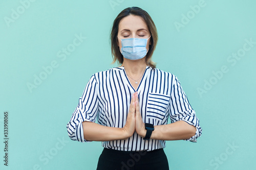 Relax and meditation. Portrait of calm middle aged woman with surgical medical mask standing and doing yoga alone. medicine and health care concept. indoor studio shot isolated on blue background. photo