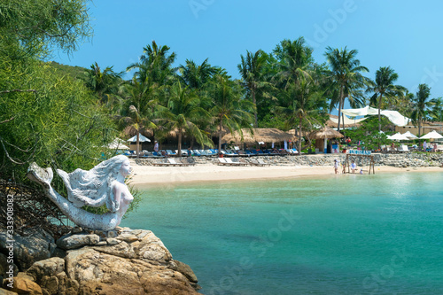 Sculpture of a mermaid on beach and thatched houses on the sand in the tropics