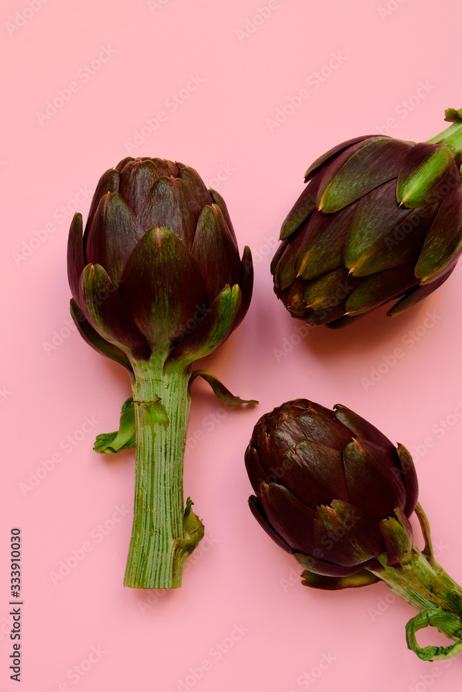 Obraz premium fresh artichokes on a pink background. layout top view. concept of seasonal vegetables. delivery of fresh vegetables