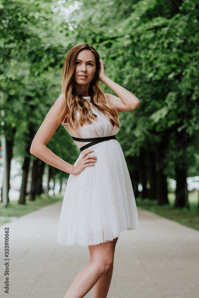 Outdoor fashion portrait of young beautiful happy smiling lady wearing white dress, stylish hairstyle, posing in park. City Outdoor fashion portrait of young beautiful happy smiling lady wearing white dress, stylish hairstyle, posing in park. City