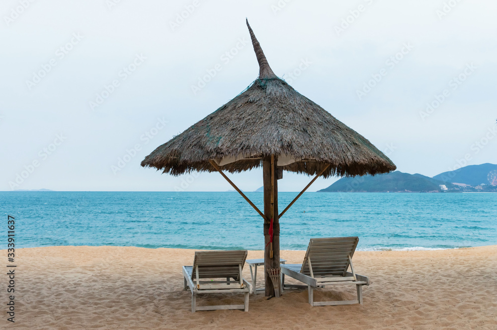 Wooden sunbeds under an umbrella on a deserted sandy beach in the evening