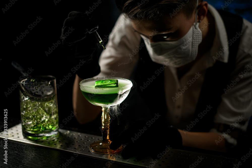 Young bartender adds ingredient to cocktail using pipette.