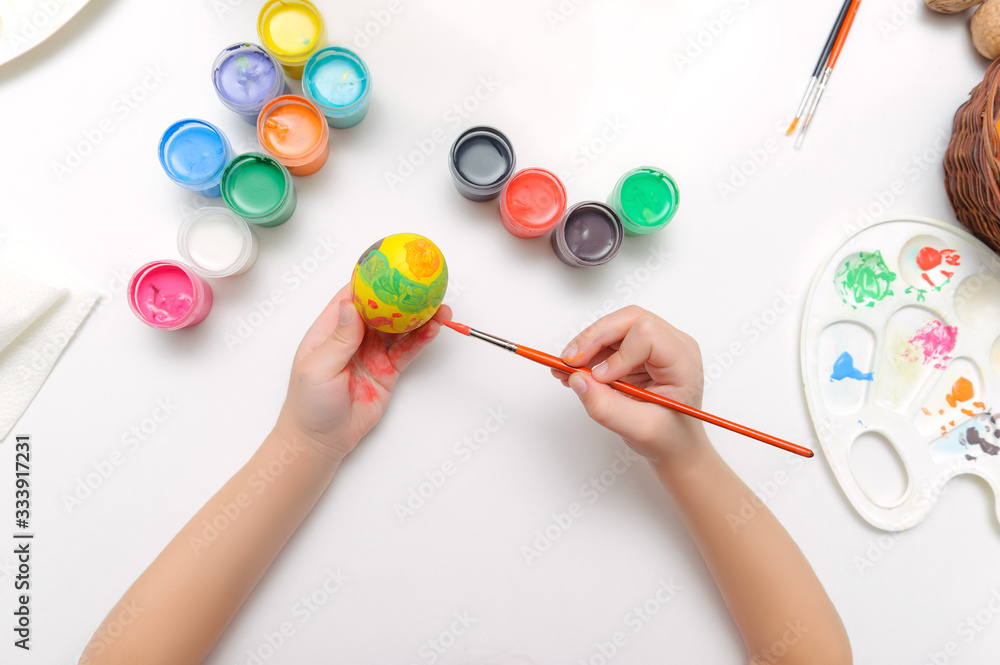 Preparing for Easter. Children paint on eggs. View from above on a white background Preparing for Easter. Children paint on eggs. View from above on a white background