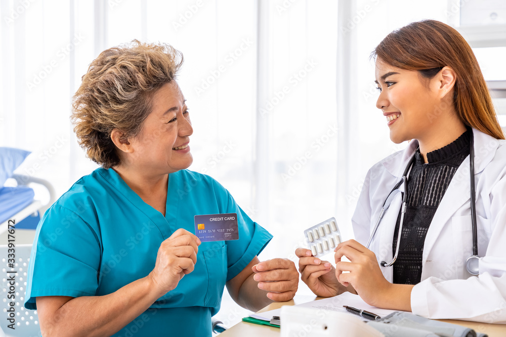 Senior Asian patient present credit card to medical doctor pharmacist for privilege and payment Senior Asian patient present credit card to medical doctor pharmacist for privilege and payment