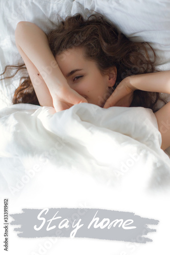 Stock photo - I stay at home awareness social media campaign and coronavirus prevention. Girl under the covers in her bed