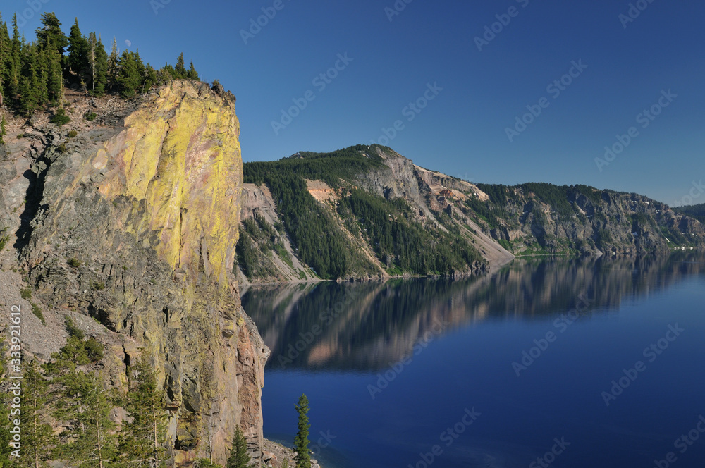 Landscape of the rugged shoreline of Crater Lake with reflections in calm water, Crater Lake National Park, Oregon, USA