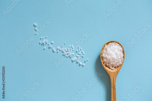 Coarse sea salt in a wooden spoon on a blue background. Ingredient for cooking and spa treatments.
