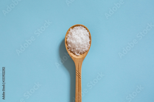 Coarse sea salt in a wooden spoon on a blue background. Ingredient for cooking and spa treatments.