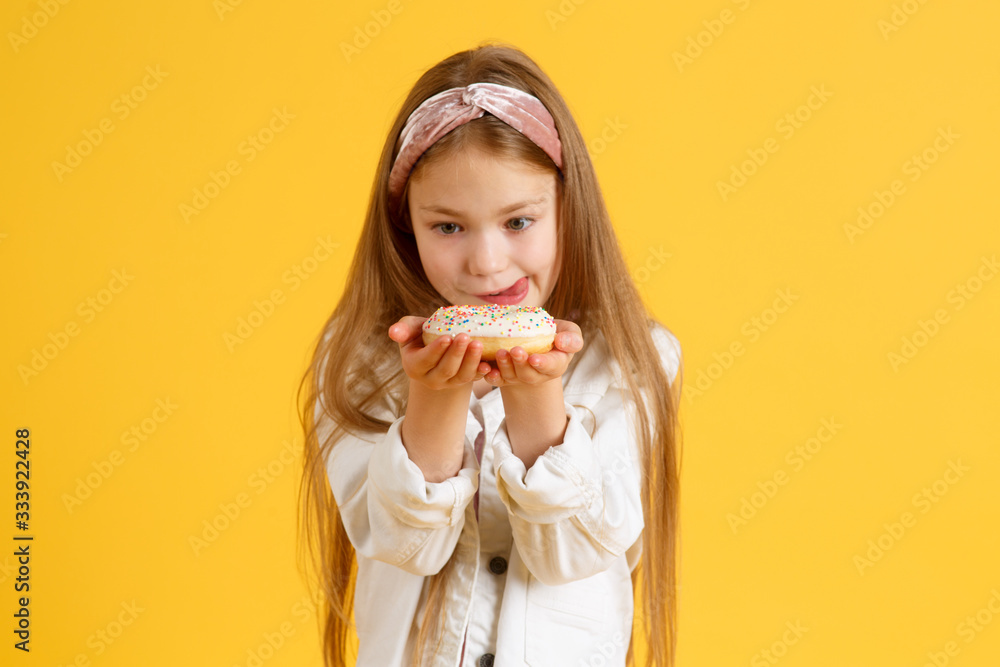 Crazy cheerful blonde girl in birthday hat smiling, having fun and looking through two red donuts on her eyes. Sweets. Yellow studio background Crazy cheerful blonde girl in birthday hat smiling, having fun and looking through two red donuts on her eyes. Sweets. Yellow studio background