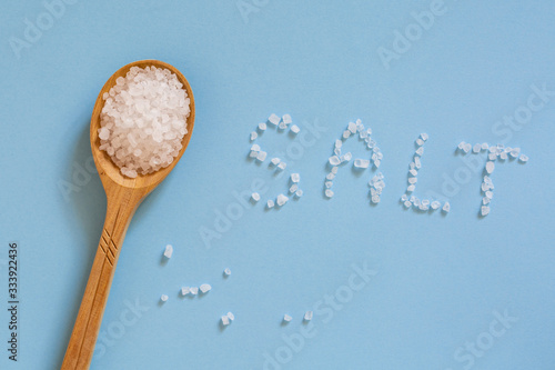 Coarse sea salt in a wooden spoon on a blue background. Ingredient for cooking and spa treatments. The inscription 