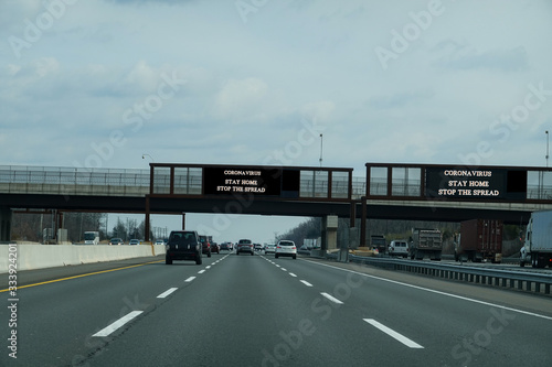 Electronic information sign over a busy multi-lane highway that says Coronavirus stay home to stop the spread