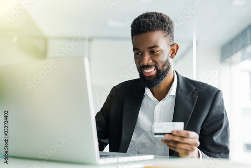 Portrait of confident young african man holding credit card with laptop paying via internet