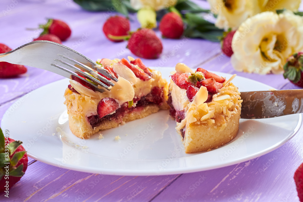 Knife and fork cutting mini tart cupcake with strawberries on plate. Close up. Knife and fork cutting mini tart cupcake with strawberries on plate. Close up.