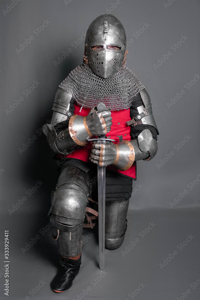 Fototapeta premium A young knight in medieval armor with a weapon in his hands kneeled.