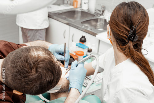 A young male dentist doctor treats a patient. Medical manipulations in dentistry  surgery. Professional uniform and equipment of a dentist. Healthcare Equipping a doctor   s workplace. Dentistry