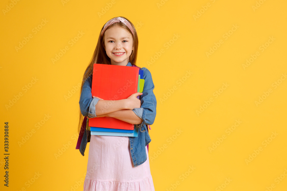 portrait of happy caucasian school girl with a book. beautiful positive girl with long red hair stand and hug her book, look at camera. she is preparing to school . isolated yellow background. portrait of happy caucasian school girl with a book. beautiful positive girl with long red hair stand and hug her book, look at camera. she is preparing to school . isolated yellow background.