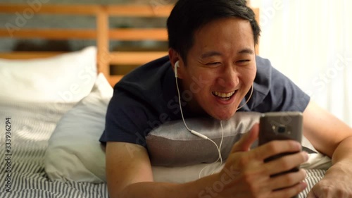 Portrait of happy 30s Asian man in casual clothing making facetime video calling with smartphone at home, waving at people on phone screen. Using conferencing meeting online app, social distancing photo